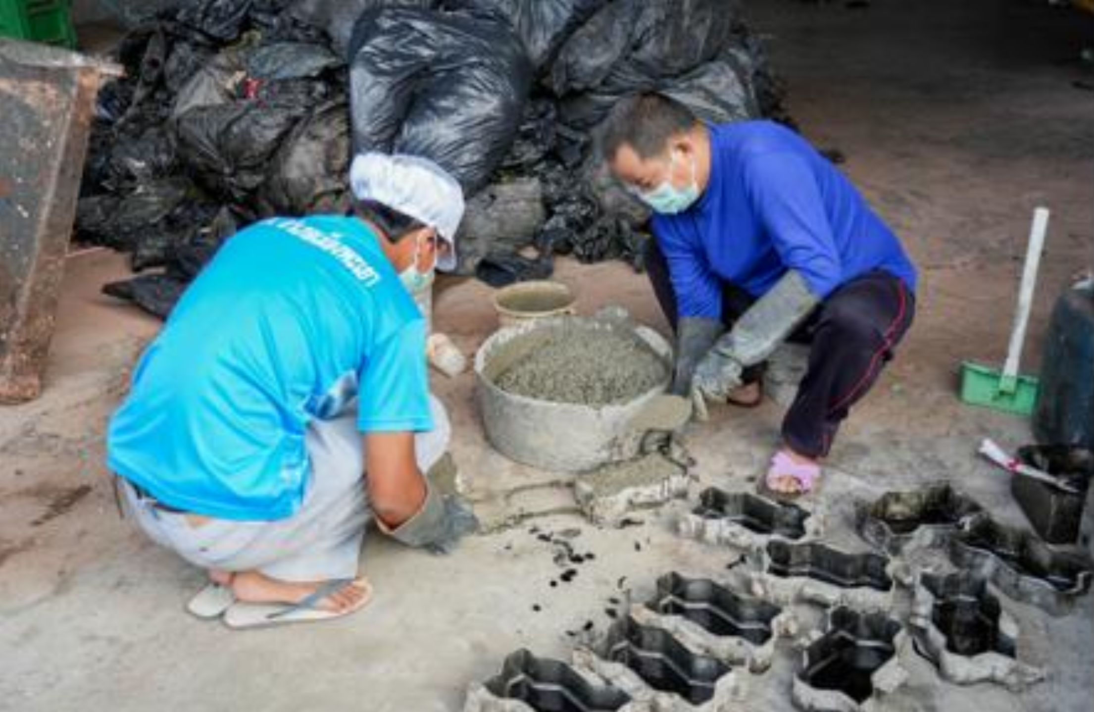 Workers molding recycled plastic paving blocks