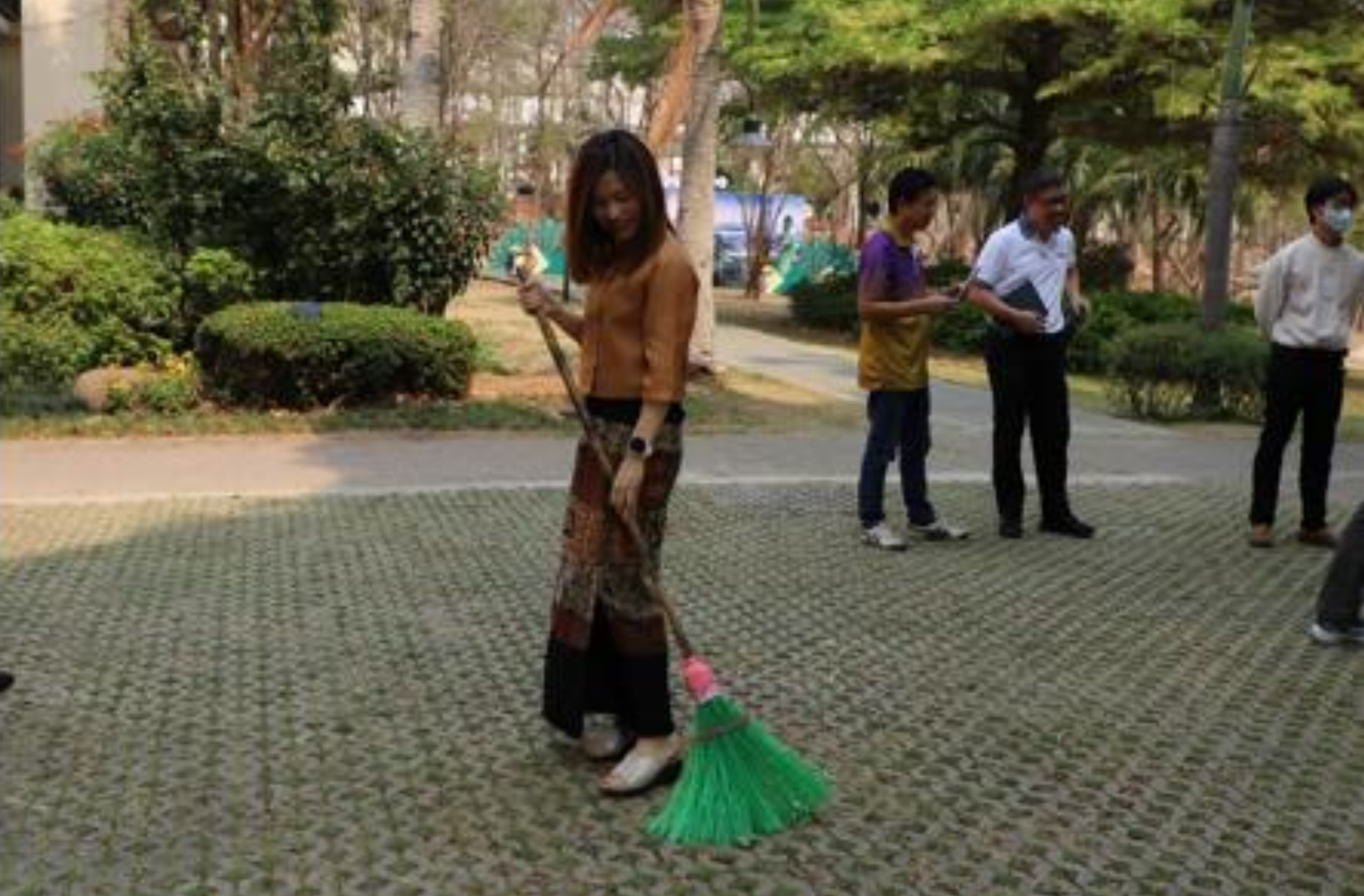 Staff using plastic-bottle brooms to sweep leaves in the university's gardens